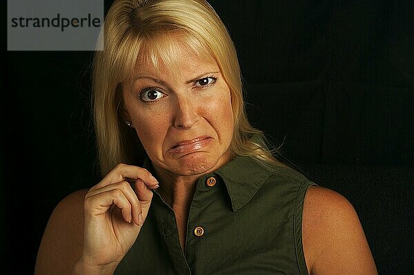 Attraktive blondhaarige  braunäugige Frau schneidet Grimassen auf einem schwarzen Hintergrund