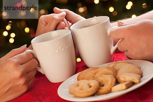 Mann und Frau teilen heiße Schokolade und Kekse vor der Weihnachtsbeleuchtung