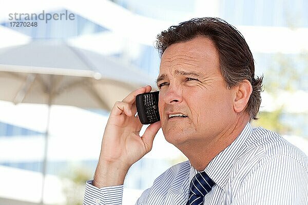 Selbstbewusster  gutaussehender Geschäftsmann lächelt  während er im Freien mit seinem Handy telefoniert