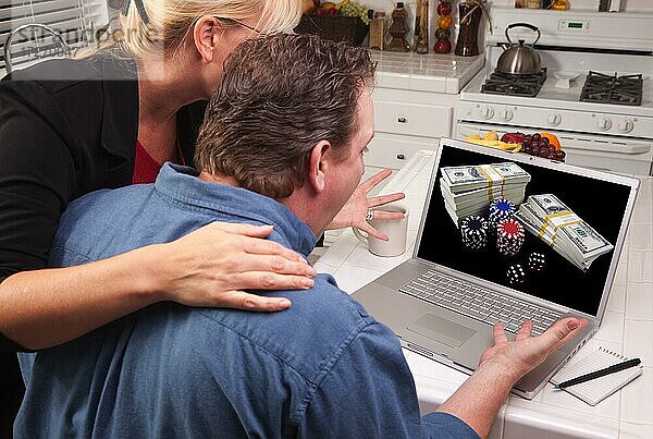 Ehepaar in der Küche mit Laptop mit Stapeln von Geld und Pokerchips auf dem Bildschirm