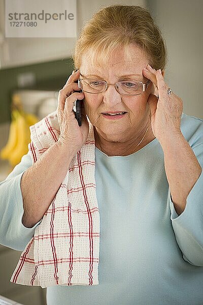 Geschockte ältere Frau am Handy in der Küche