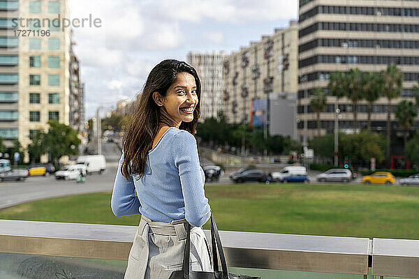 Lächelnde schöne Geschäftsfrau steht am Geländer  während die Stadt im Hintergrund