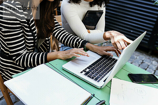 Weibliche Kollegen benutzen einen Laptop  während sie auf einem Tisch in einem Café sitzen