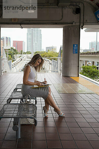 Geschäftsfrau beim Schreiben auf einer Bank am Bahnhof sitzend