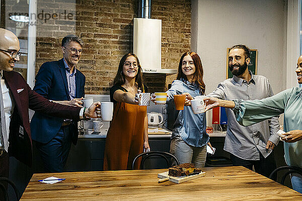 Lächelnde männliche und weibliche Unternehmer  die am Tisch in der Büroküche Kaffee rösten