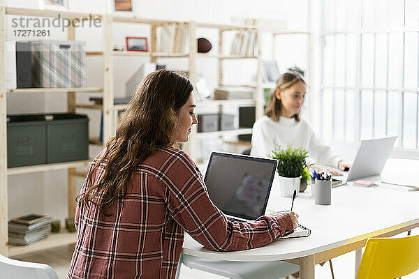 Frau  die einen Laptop benutzt  mit einer Geschäftsfrau  die im Hintergrund im Büro sitzt