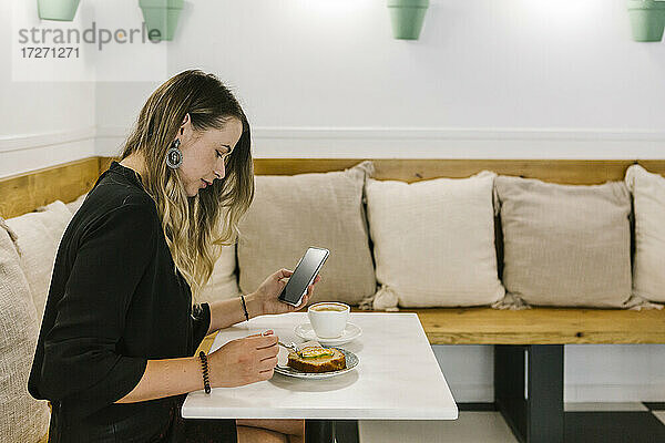 Geschäftsfrau  die ein Mobiltelefon benutzt  während sie in einem Café Kuchen isst