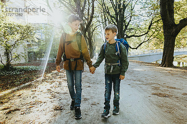 Junge hält die Hand seines jüngeren Bruders bei einem Spaziergang in einem öffentlichen Park an einem sonnigen Tag