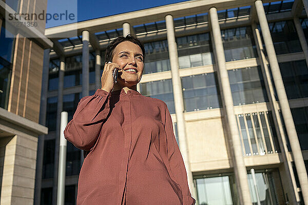 Geschäftsfrau  die mit ihrem Smartphone telefoniert  während sie an einem Gebäude steht
