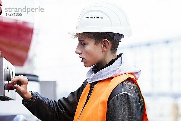Männlicher Jugendlicher  der auf einer Baustelle Maschinen bedient