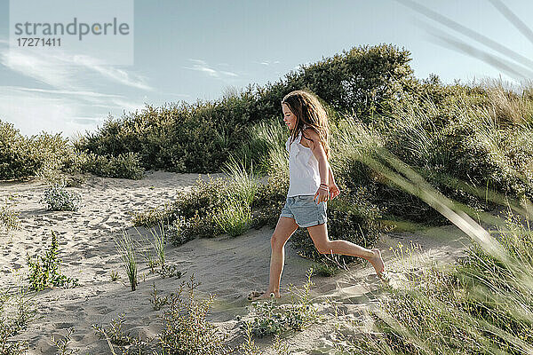 Mädchen läuft auf Sand am Strand während eines sonnigen Tages