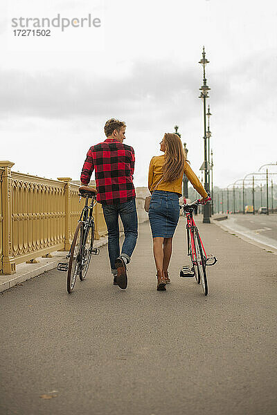 Lächelndes heterosexuelles Paar mit Fahrrad auf dem Gehweg in der Stadt