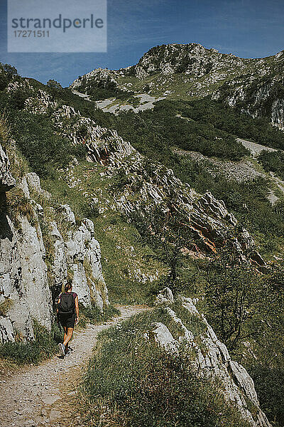 Frau  die an einem sonnigen Tag auf einem Wanderweg bei einer Felsformation spazieren geht