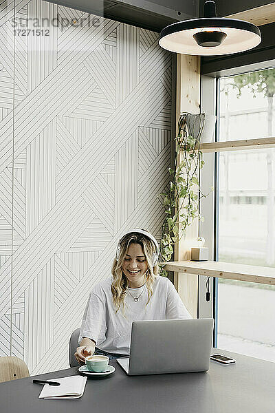 Junge Frau schaut auf eine Kaffeetasse  während sie in einem Café sitzt und einen Laptop benutzt