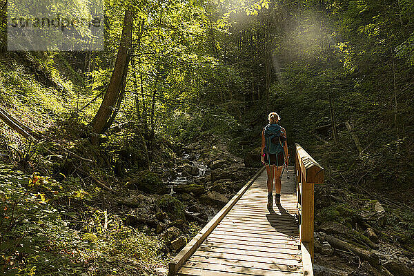Wanderin beim Überqueren einer Holzbrücke  die sich im Sommer über einen Waldbach spannt
