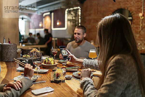 Junge Frau  die mit ihrem Handy ein Foto vom Essen macht  während sie mit Freunden im Restaurant sitzt