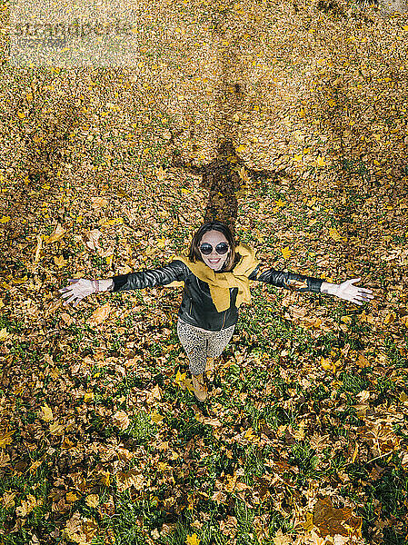 Lächelnde schöne Frau mit ausgestreckten Armen genießt den Herbst im Park