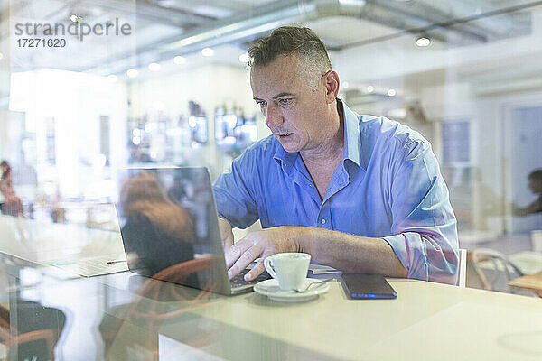 Männlicher Unternehmer  der einen Laptop benutzt  während er mit einem Kaffee im Café sitzt