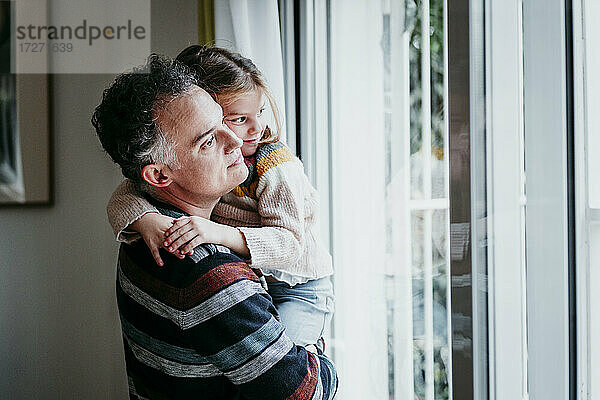 Vater trägt Tochter am Fenster stehend nach Hause