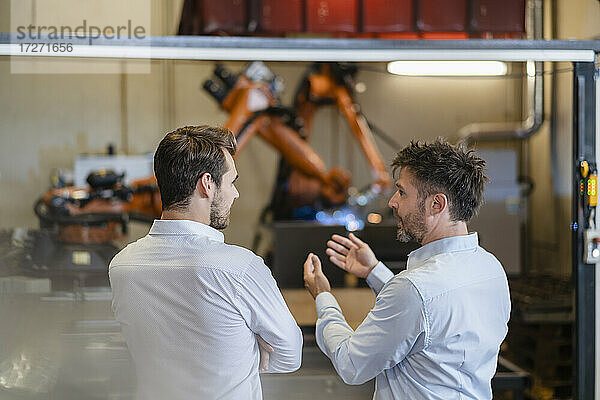 Geschäftsmann diskutiert  während er vor einer Roboterarm-Maschine in einer modernen Fabrik steht