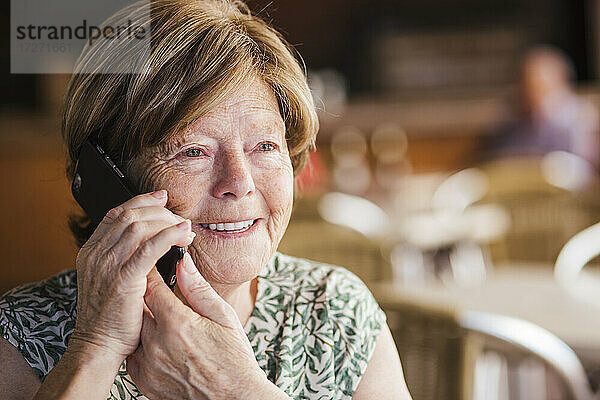 Lächelnde Frau  die in einem Café sitzt und mit ihrem Handy telefoniert