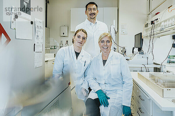 Mitarbeiter lächelnd  während sie mit einem Wissenschaftler im Hintergrund in einem Labor sitzen