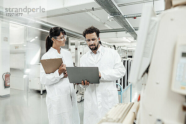 Eine Wissenschaftlerin sieht einen männlichen Kollegen an  der einen Laptop im Labor benutzt