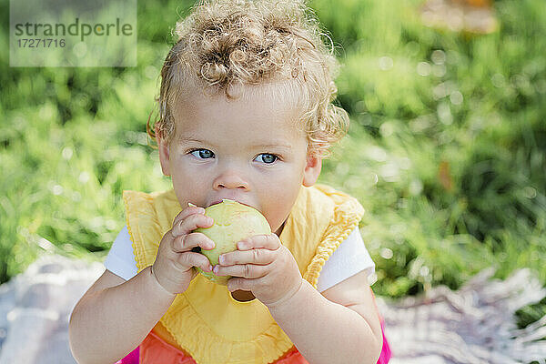 Süßes Baby Mädchen essen Obst  während auf Gras im Park sitzen