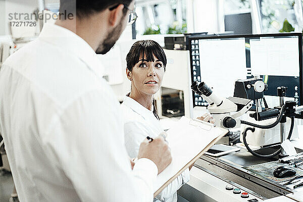 Geschäftsfrau schaut auf Geschäftsmann mit Klemmbrett im Labor stehend