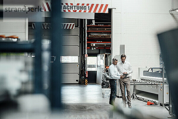 Männliche Ingenieure diskutieren über ein digitales Tablet  während sie in einer Fabrik stehen