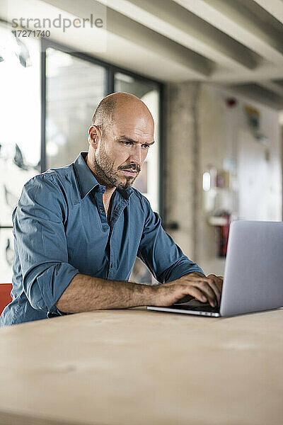Geschäftsmann arbeitet am Laptop  während er am Tisch im Büro sitzt