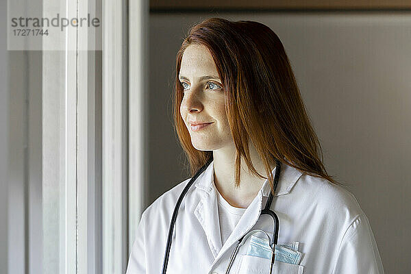 Lächelnde junge Ärztin schaut durch ein Fenster