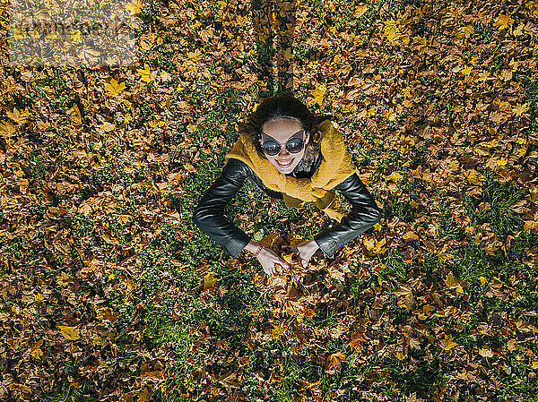 Glückliche Frau hält trockene Blätter  während sie sich im Herbst im Park vergnügt