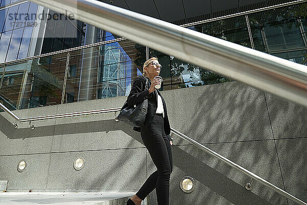 Ältere Frau mit Kaffeetasse  die auf einer Treppe gegen ein Gebäude läuft
