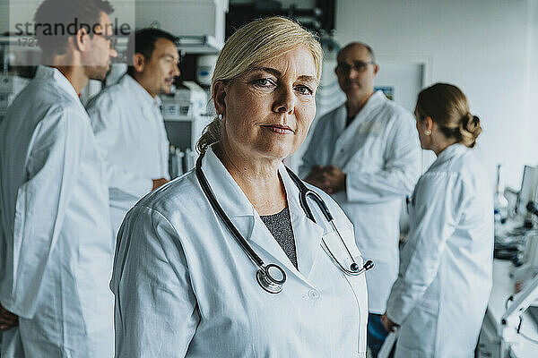 Lächelnde Wissenschaftlerin  die wegschaut  während sie mit einem Mitarbeiter im Hintergrund im Labor steht