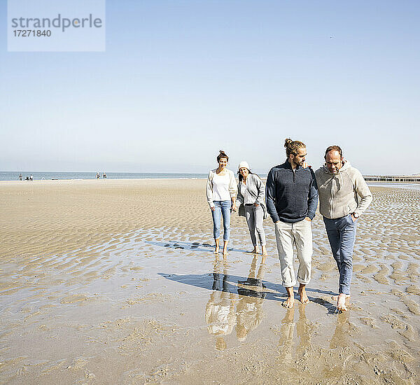 Männer unterhalten sich beim Gehen mit Frauen im Hintergrund am Strand
