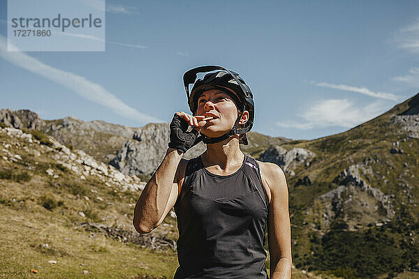 Frau mit Fahrradhelm isst einen Keks  während sie an einem Berg im Somiedo-Naturpark steht  Spanien