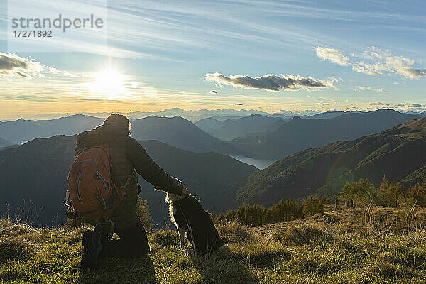 Wanderer kniend beim Streicheln des Hundes auf dem Berggipfel bei Sonnenuntergang