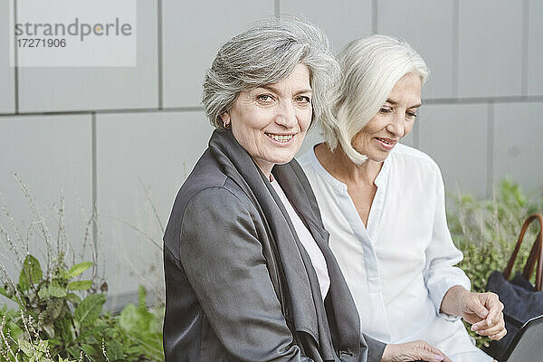 Lächelnde Geschäftsfrau  die mit einer Frau an einem Gebäude sitzt
