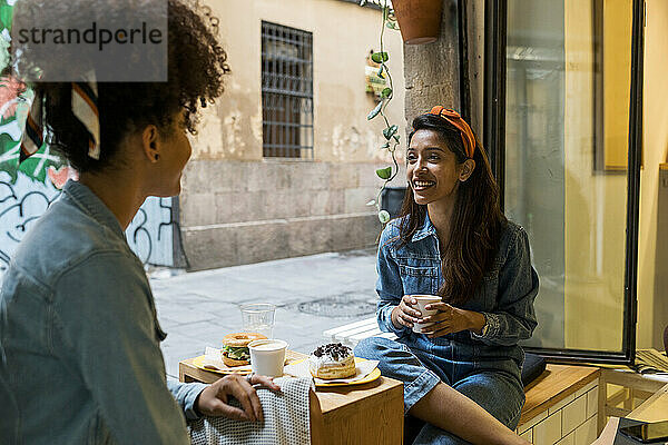 Freunde lächelnd beim Essen und Trinken im Café sitzend