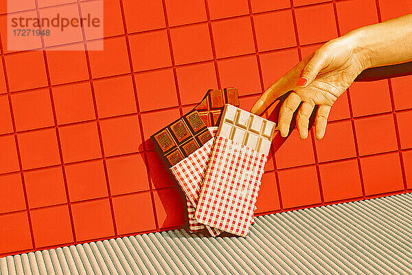 Mittlere erwachsene Frau wählt mit der Hand Schokolade aus  die in einer Reihe vor einer roten Kachelwand aufbewahrt wird