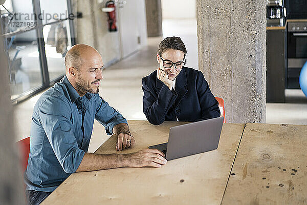 Unternehmer  die einen Laptop benutzen  während sie am Tisch im Büro sitzen