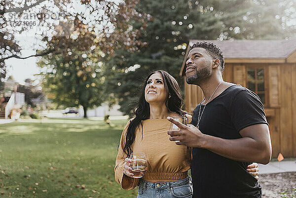 Mann und Frau mit Weinglas  die in einem Hinterhof stehen und nach oben schauen