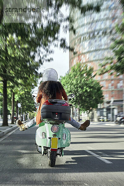 Unbekümmerte Frau auf einem Motorroller in der Stadt an einem sonnigen Tag
