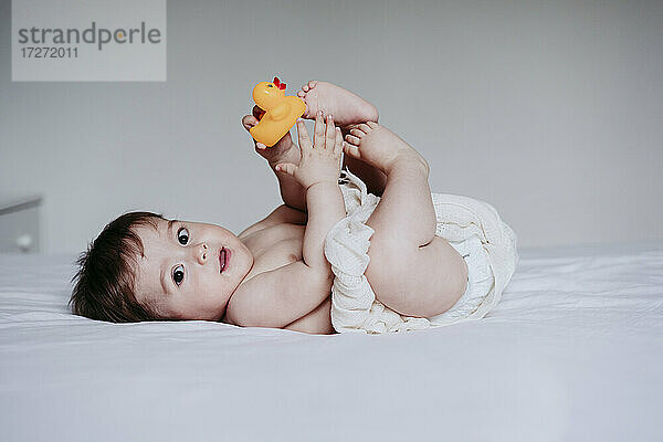Süßes Baby Junge spielt mit Ente Spielzeug  während auf dem Bett zu Hause liegen