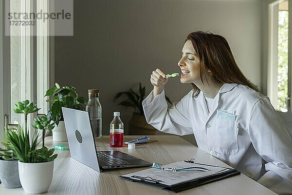 Junge Zahnärztin unterrichtet Zähneputzen per Videoanruf auf dem Laptop zu Hause