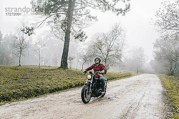 Männlicher Motorradfahrer auf einem unbefestigten Weg bei nebligem Wetter