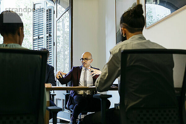 Geschäftsmann gestikuliert bei der Diskussion mit Kollegen am Tisch im Büro
