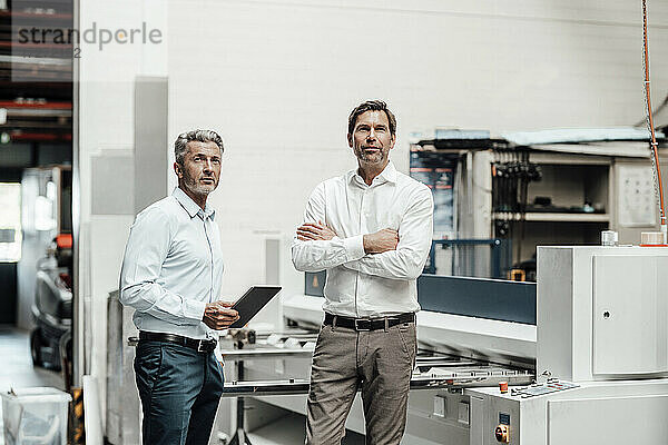 Männliche Ingenieure schauen weg  während sie an einer Maschine in einer Fabrik stehen
