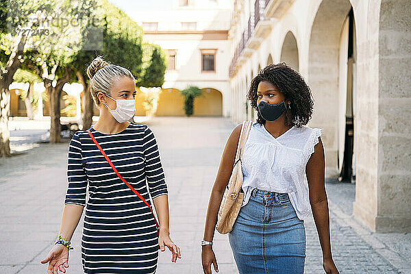 Frauen mit Gesichtsmaske unterhalten sich beim Spaziergang in der Stadt
